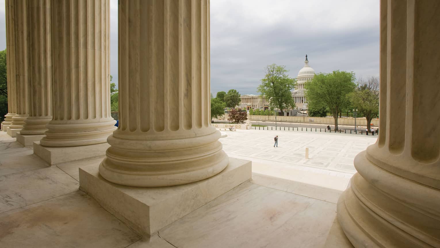 View of Washington DC Capitol Dome from between large white pillars on Supreme court house steps