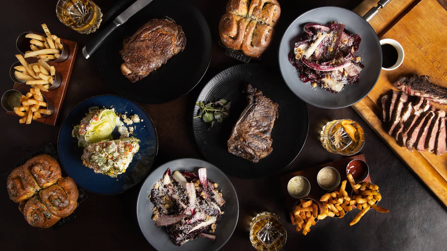 Multiple plates of food, including french fries, steak and bread rolls.