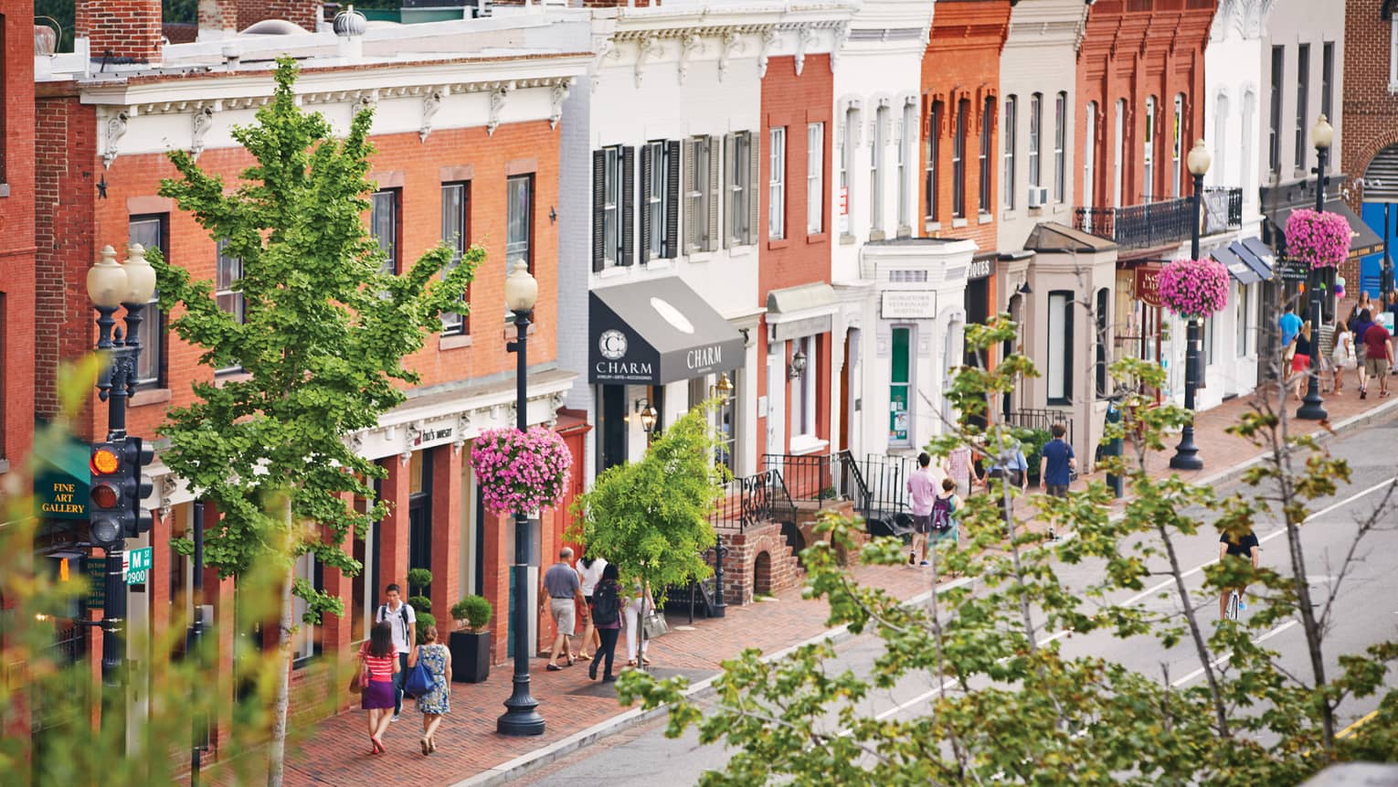 View past trees over summer street where pedestrians walk by historic brick storefronts