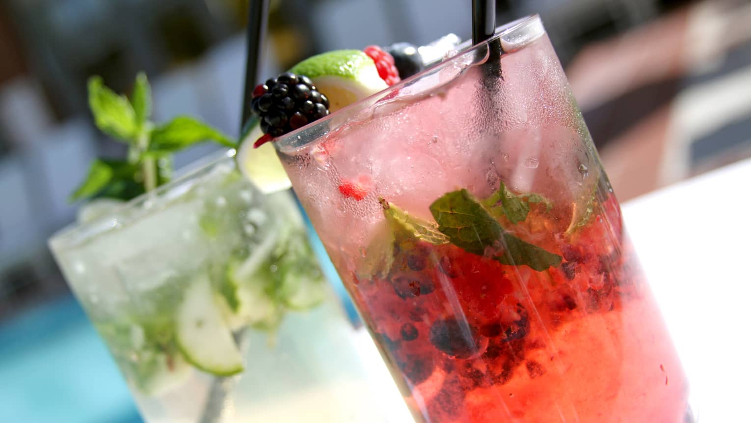 Two different mojitos: one pink garnished with fruit, one with cucumber and mint