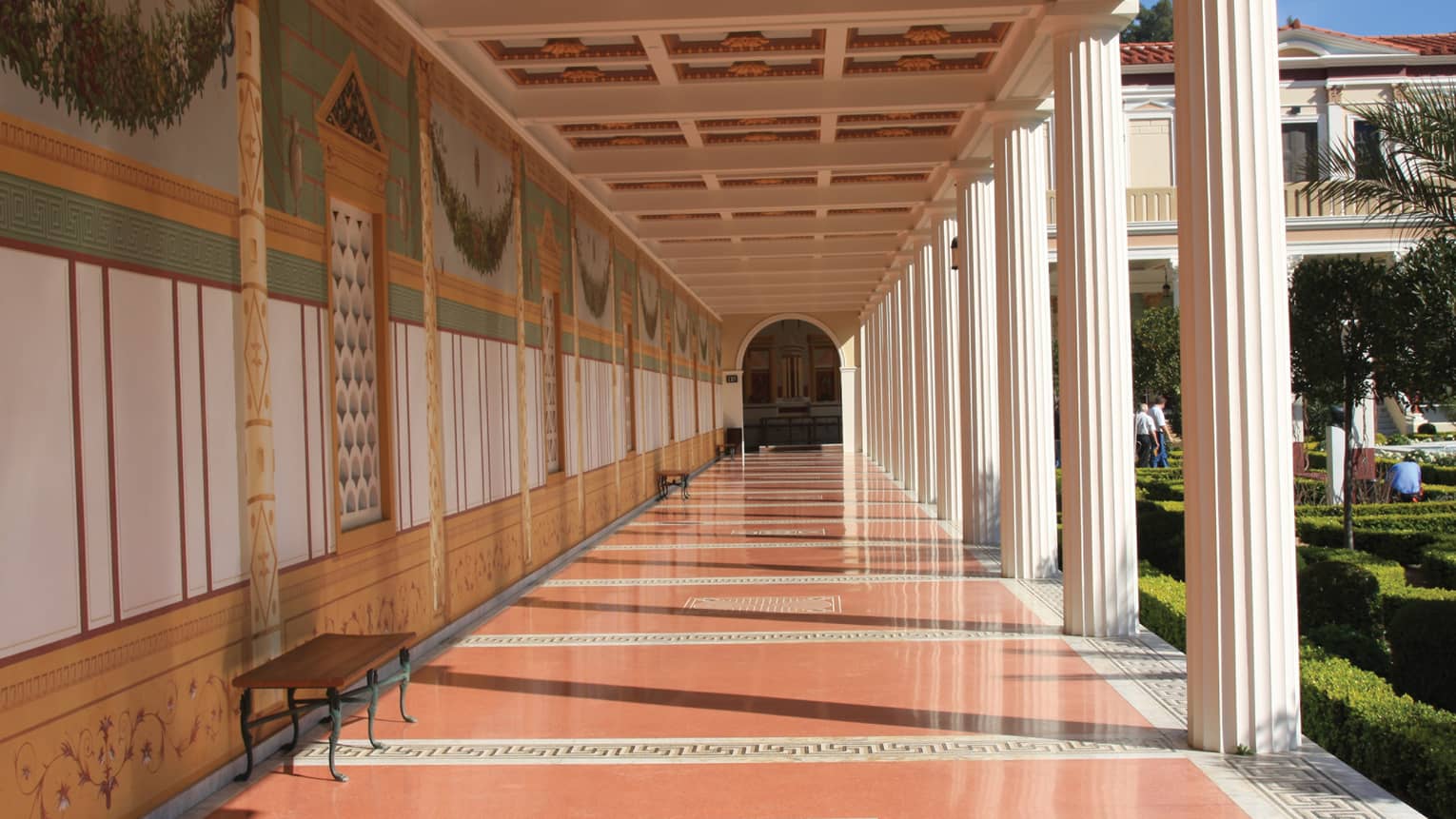 A long hallway with orange floors and columns on the side leading to an arched doorway.