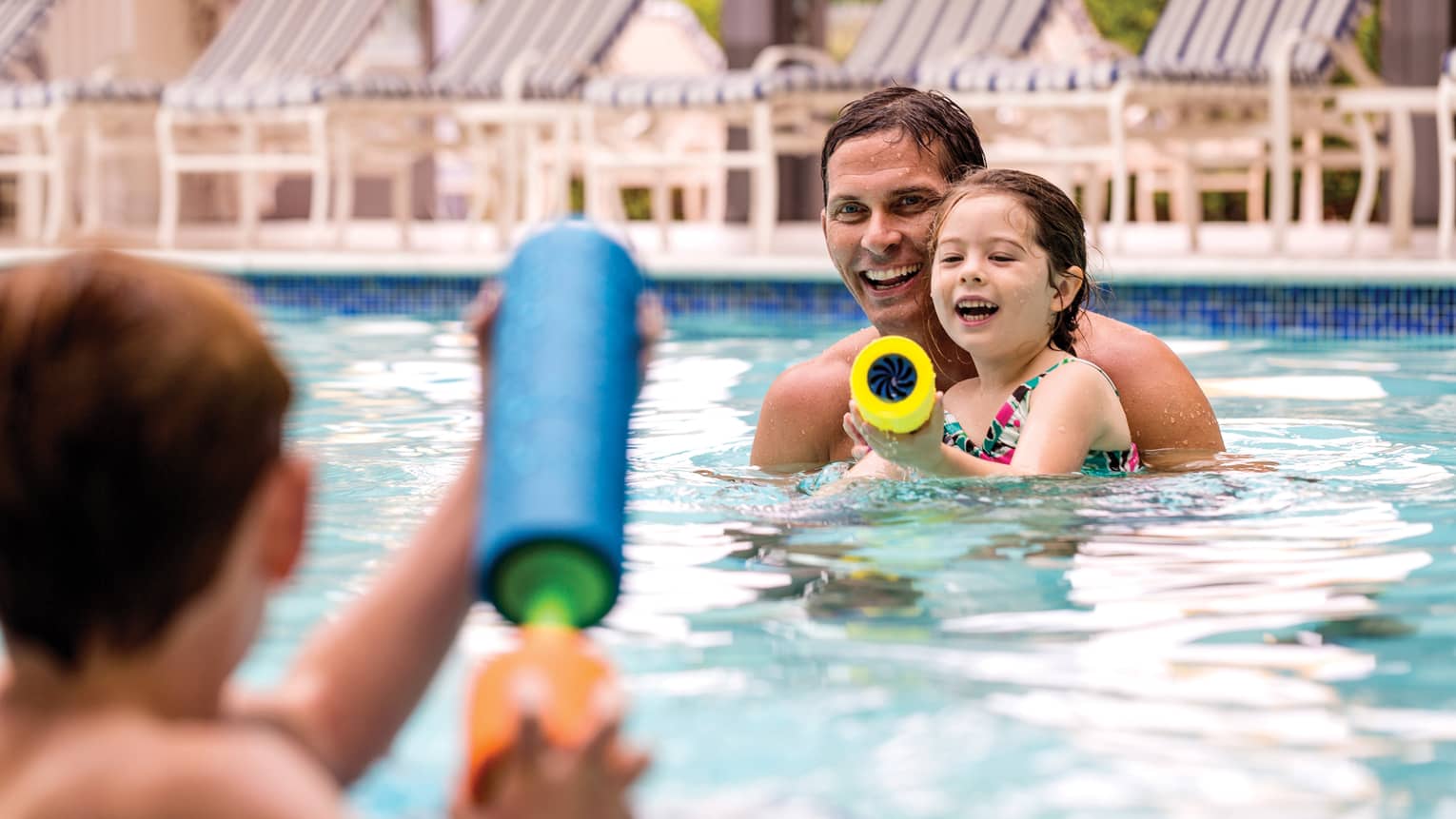Smiling family swimming in outdoor pool squirt water guns at each other