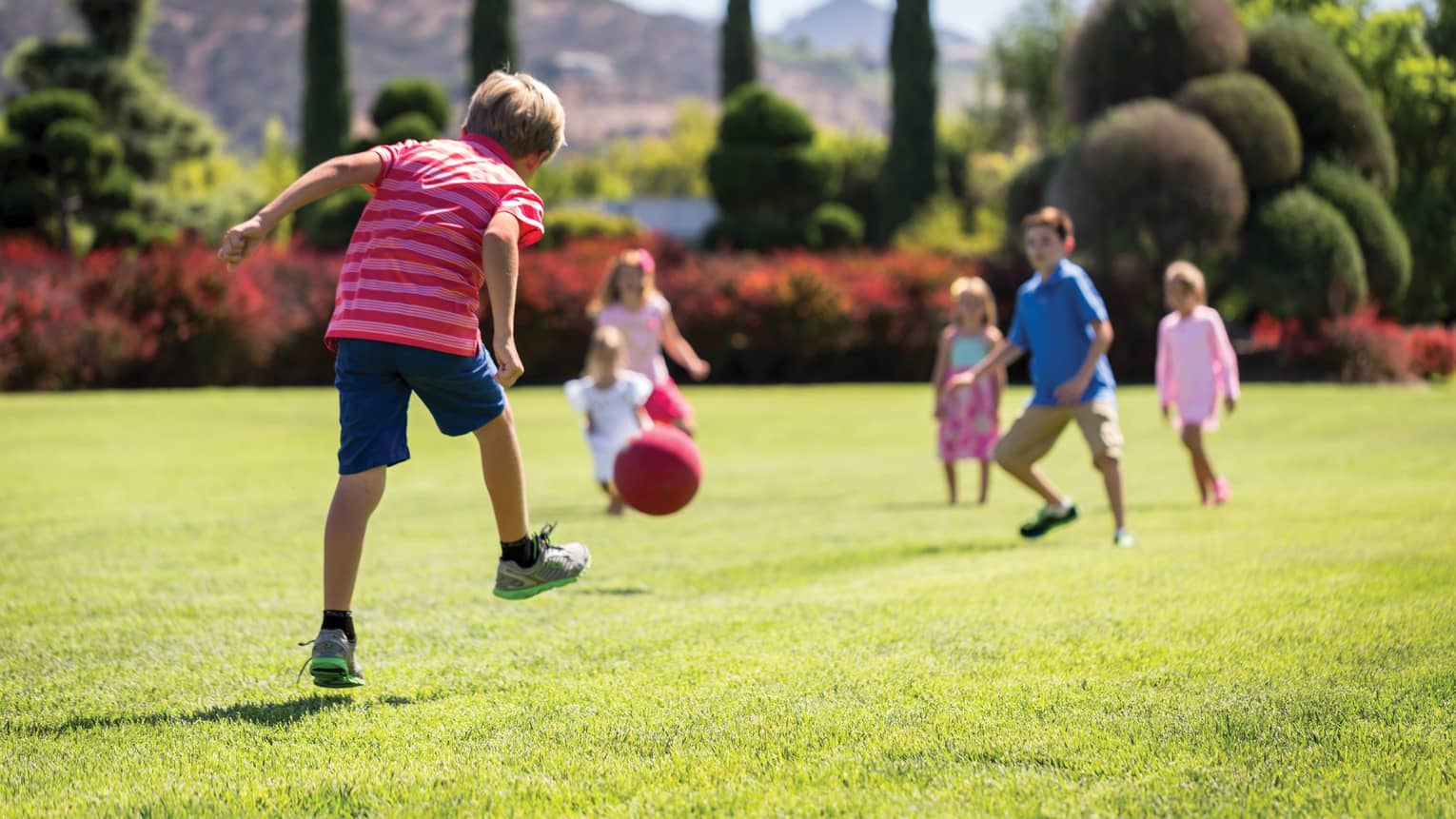 Kids playing with a ball on green grass outside.