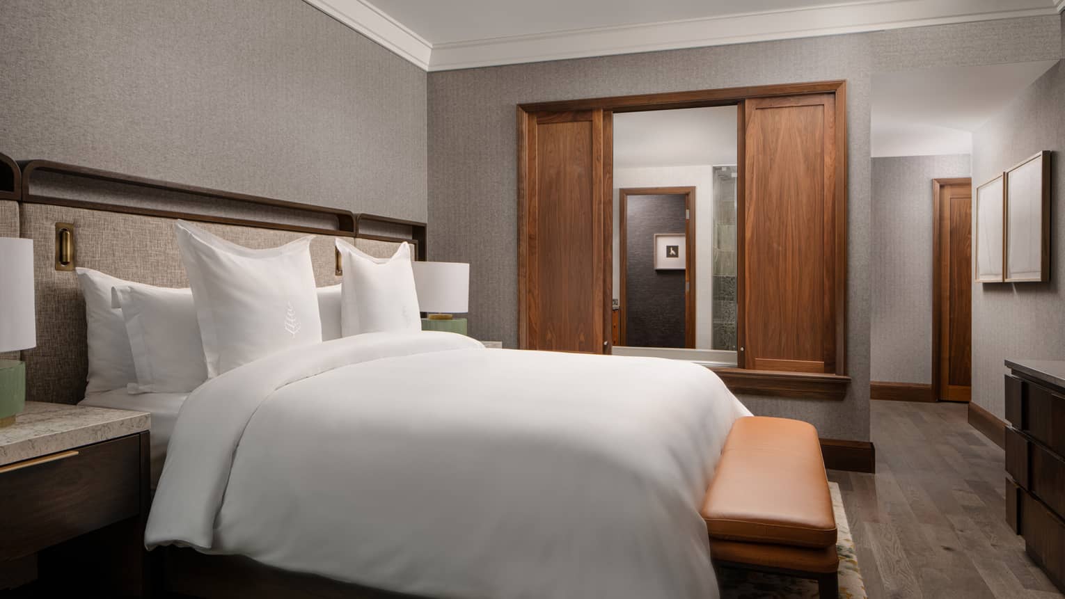 Bedroom with king bed, bench, sliding wooden doors to bathroom