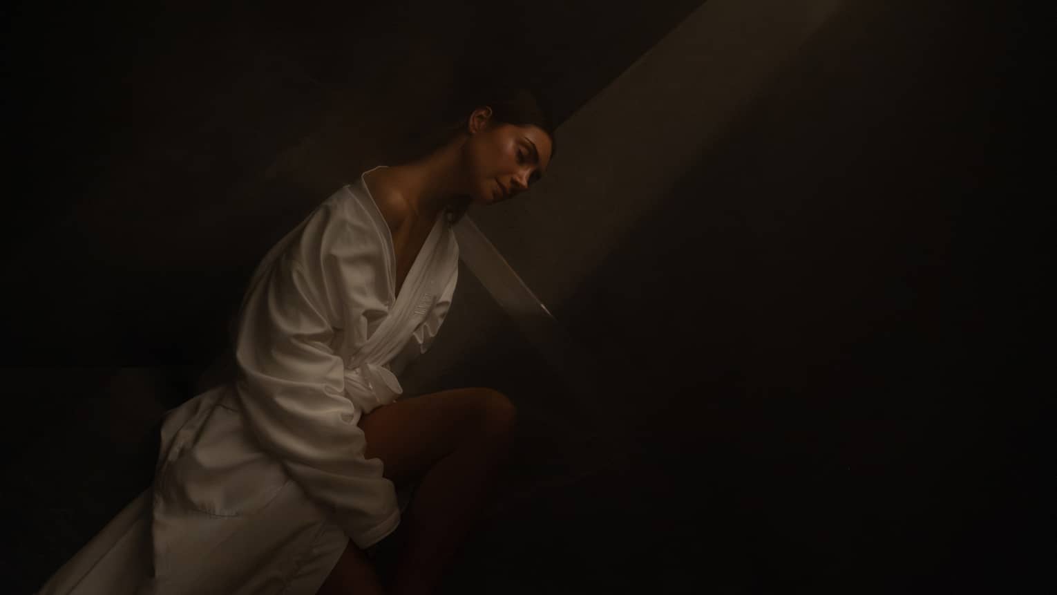 Guest wearing white robe sits in a dimly lit eucalyptus-infused steam room