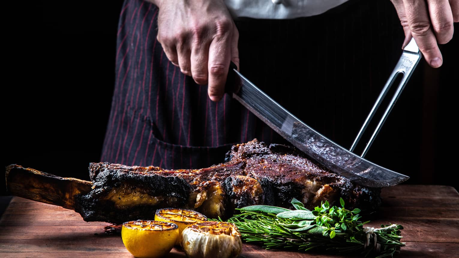 Close-up of chef slicing large rack of grilled meat, vegetables with butcher knives