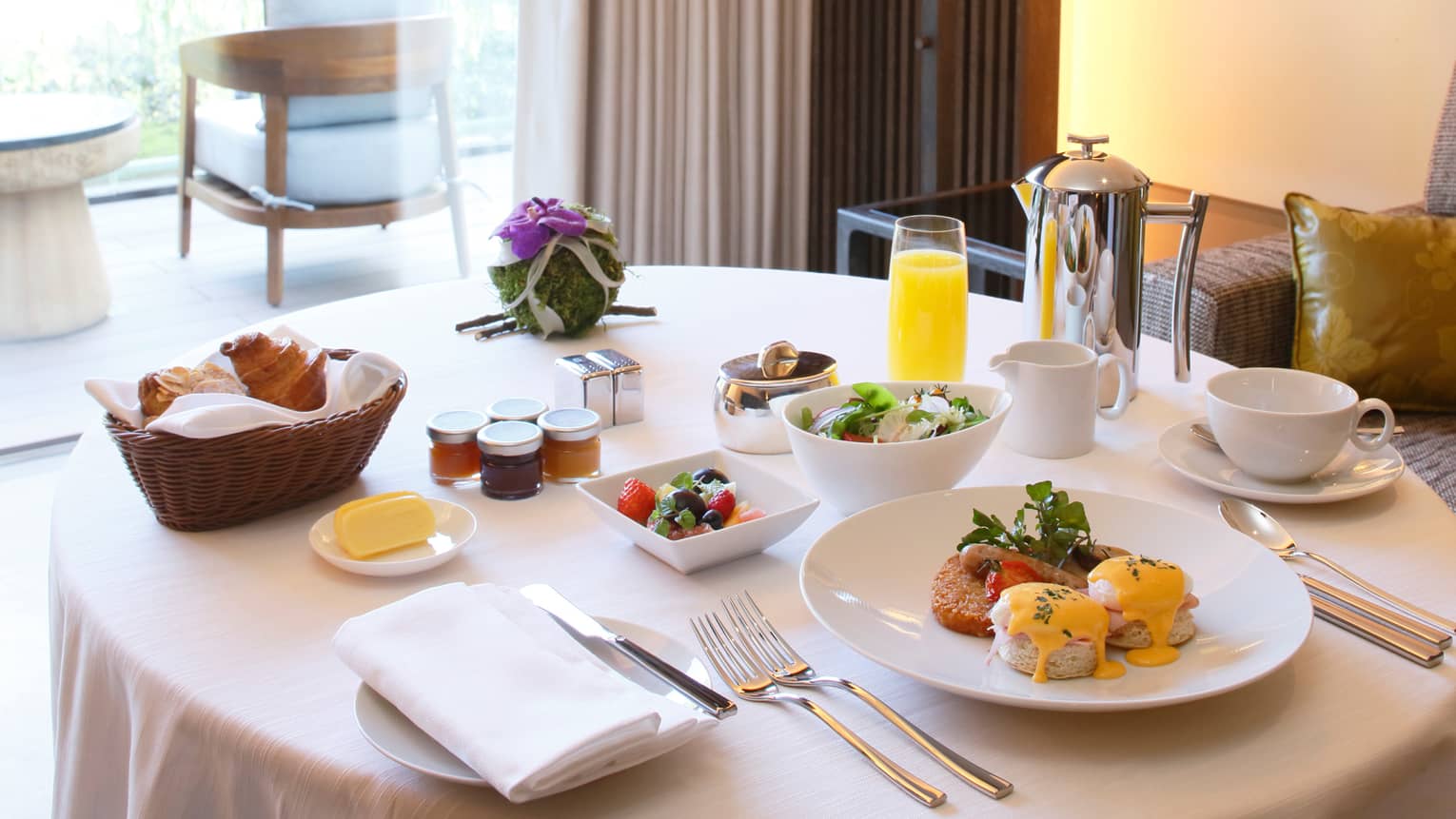 Eggs benedict brunch on plate, fruit and salad in bowls