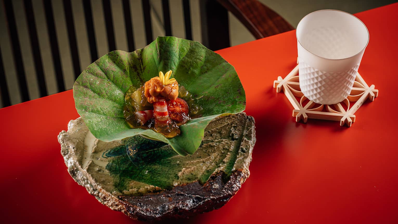 Kuruma prawn and eggplant served in a green leaf-shaped bowl on a bright red table