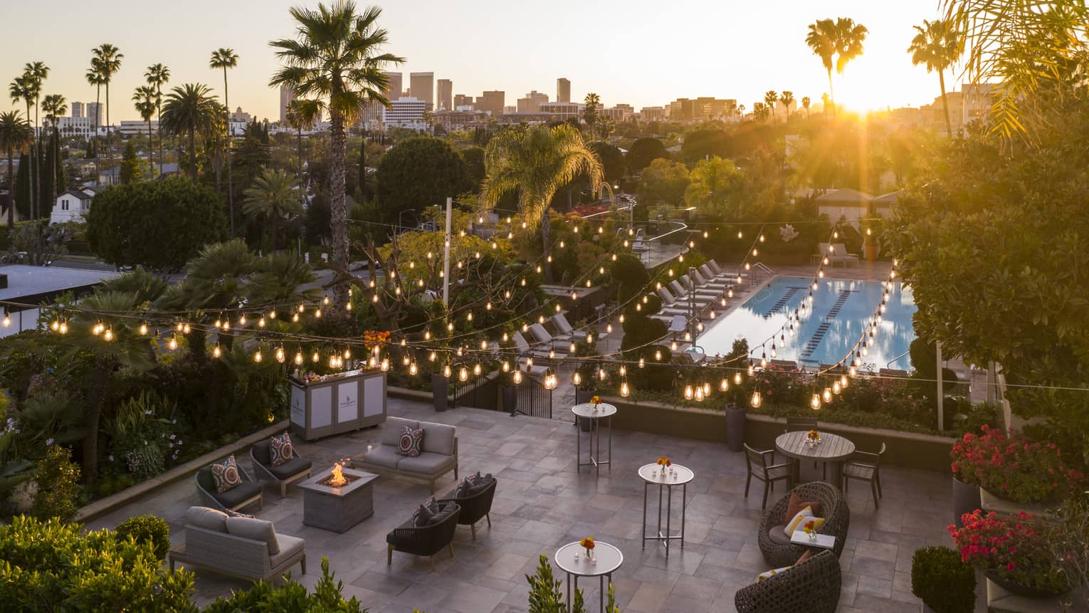 An outdoor seating area with hanging fairy lights and a fire pit near chairs and small tables.