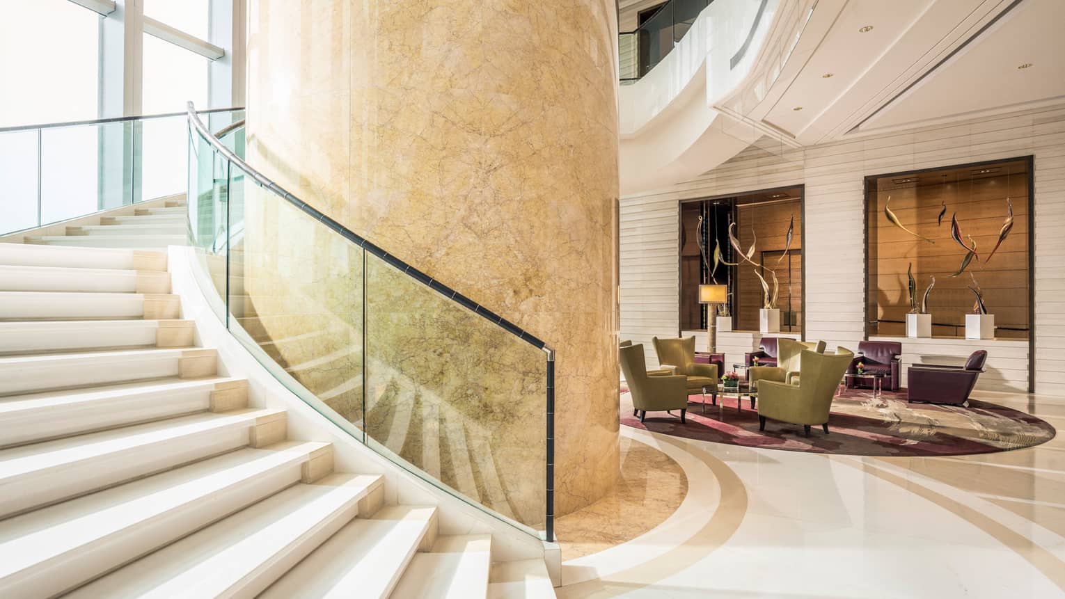 Large beige marble pillar, sweeping staircase with glass balcony in Four Seasons Hotel Hong Kong lobby