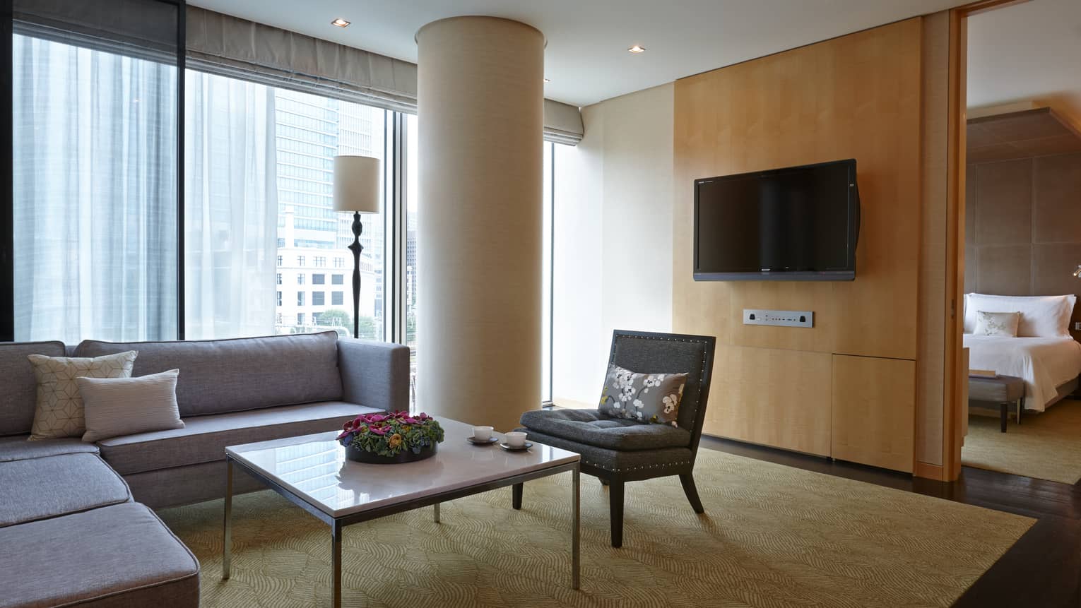 Executive Suite living room L-shaped grey sofa chair by white pillar, TV, bedroom door