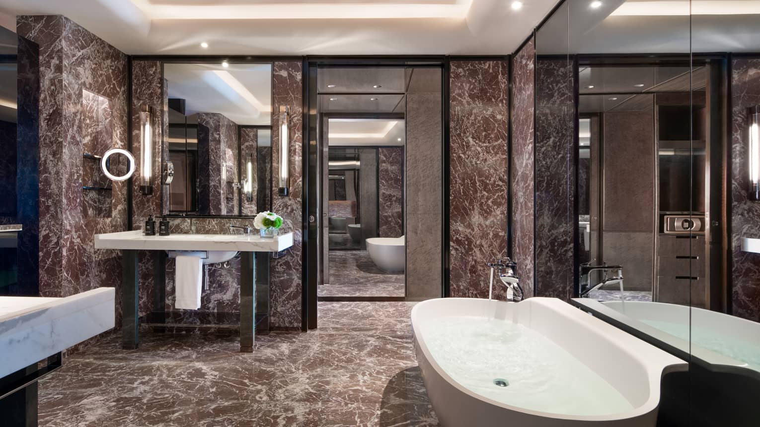 Guest bathroom with chocolate marble walls and floors, single vanity, large soaking tub, lighted wall sconces