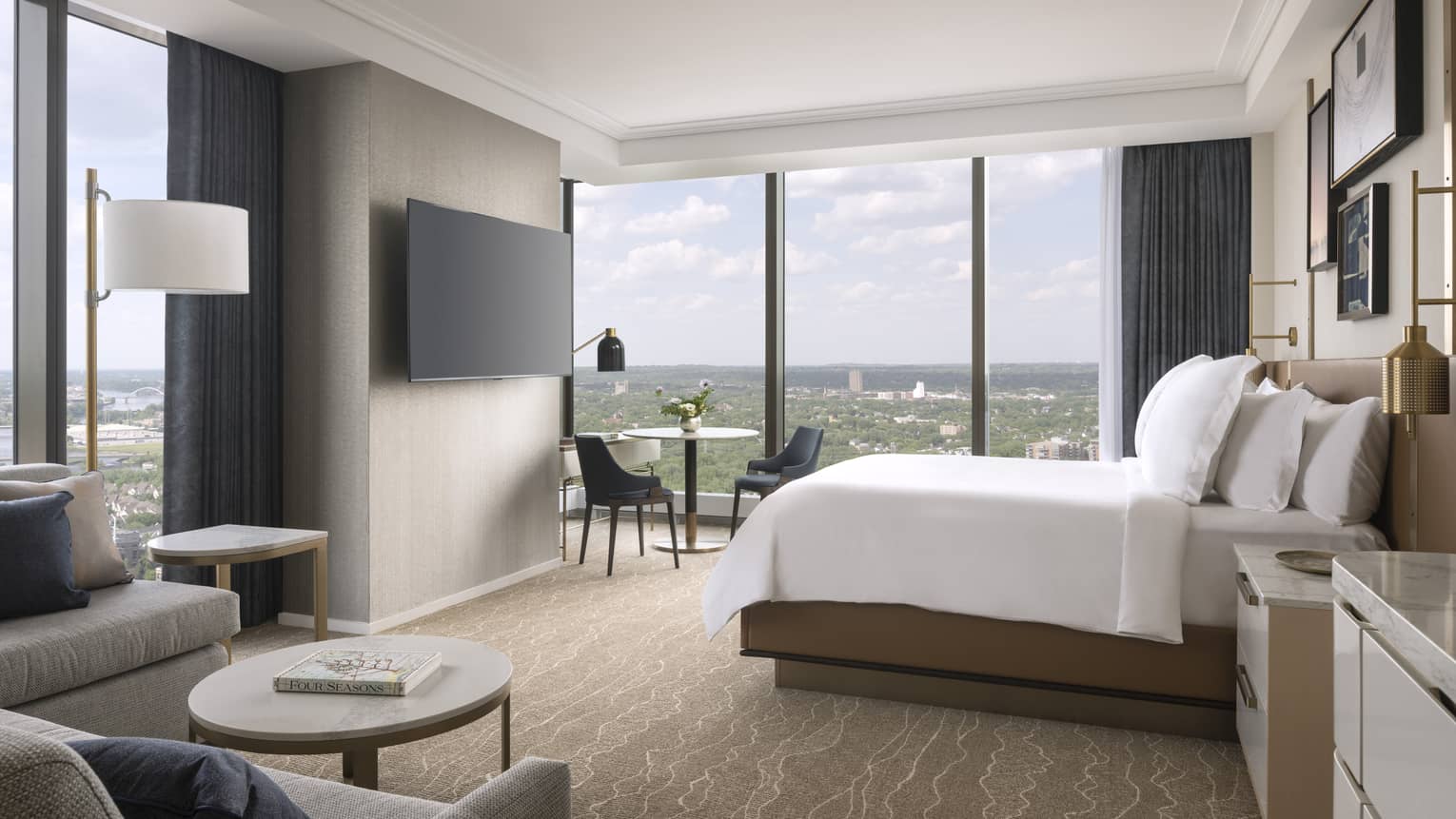 Hotel room with king bed, sofa, wall-mounted TV and wall of windows