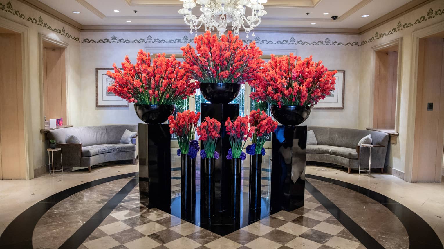 Hotel lobby, large red floral arrangements in black vases under crystal chandelier