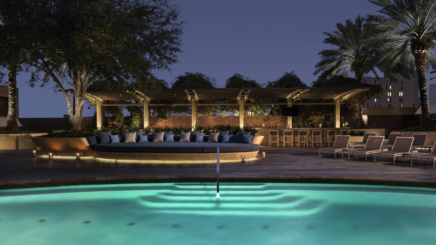 Outdoor swimming pool with lights and patio with large banquette at night