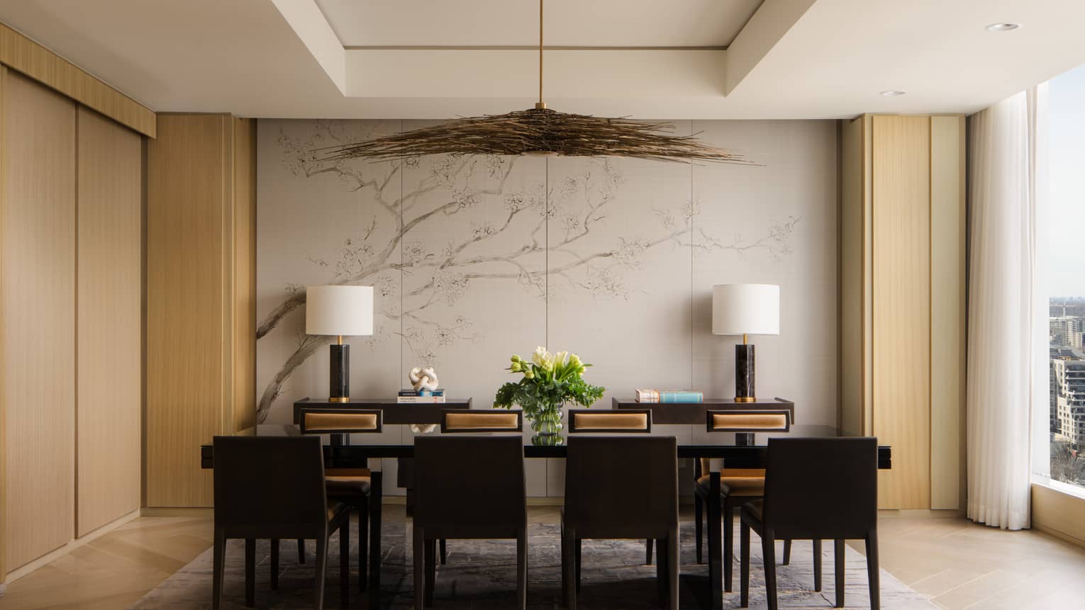 A sophisticated dining room setup with a large black table, eight chairs and a centrepiece of fresh flowers