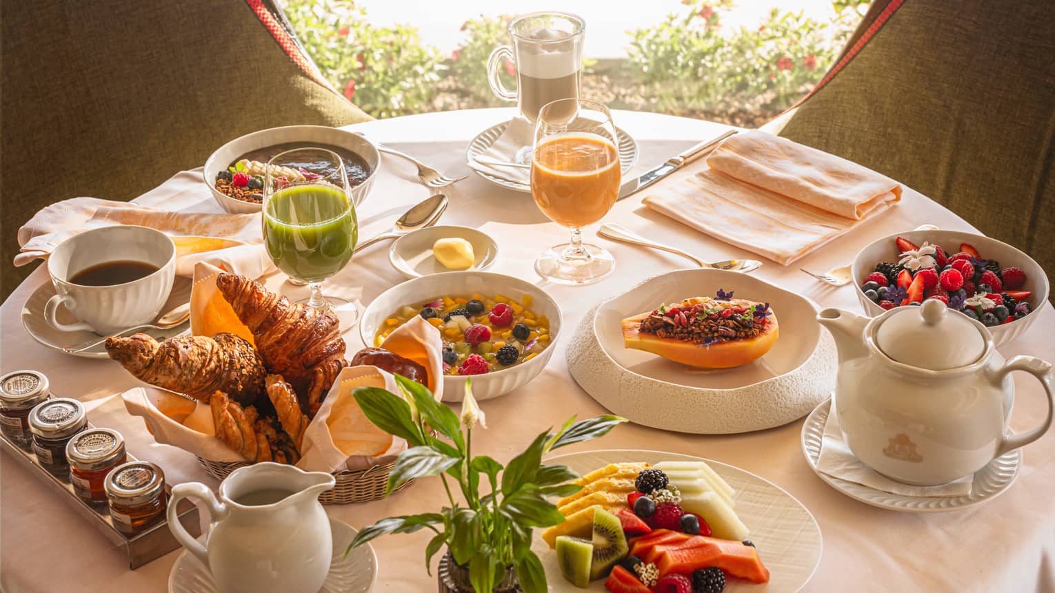 A round table in front of a window, set with an array of brunch dishes and beverages