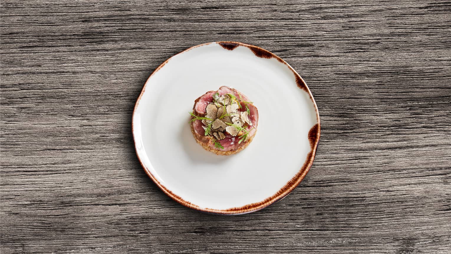 Wagyu with buckwheat, a sauce and chervil on a white plate.