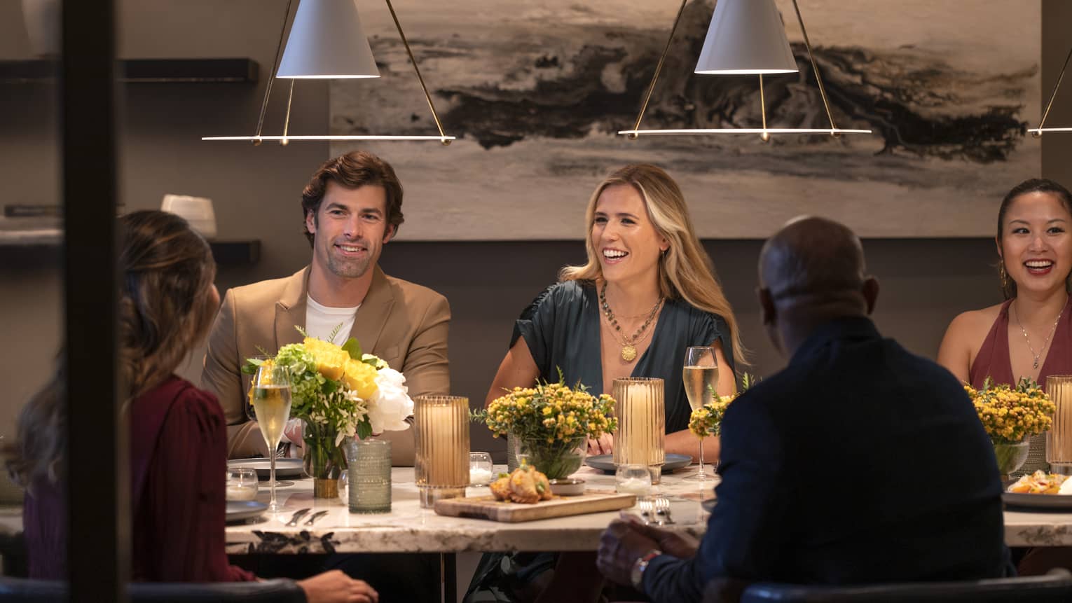 Guests sitting at a table and smiling at each other at a restaurant with overhead lighting