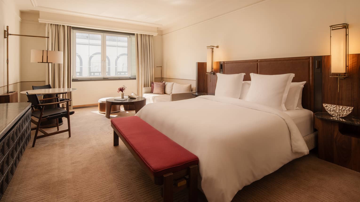 Hotel room featuring a king bed, red bench, lounge area and window