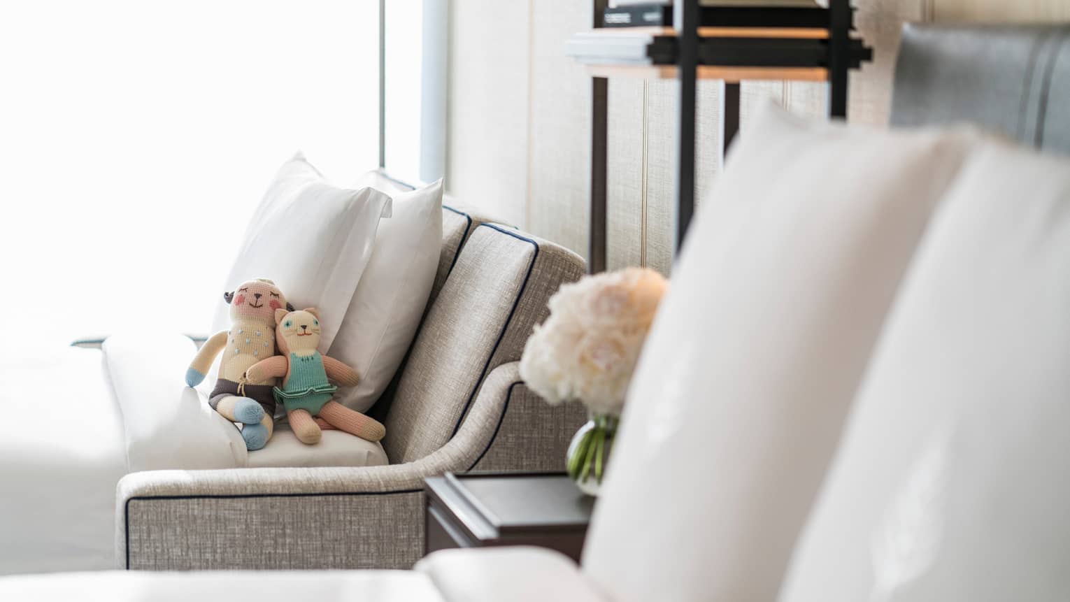 Two small stuffed toys rest against pillows on pull-out sofa beside hotel bed