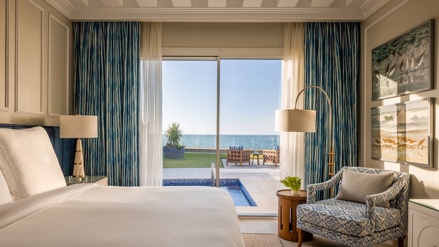 One-Bedroom Beach Villa bedroom with king bed, patterned armchair, sliding glass door to pool