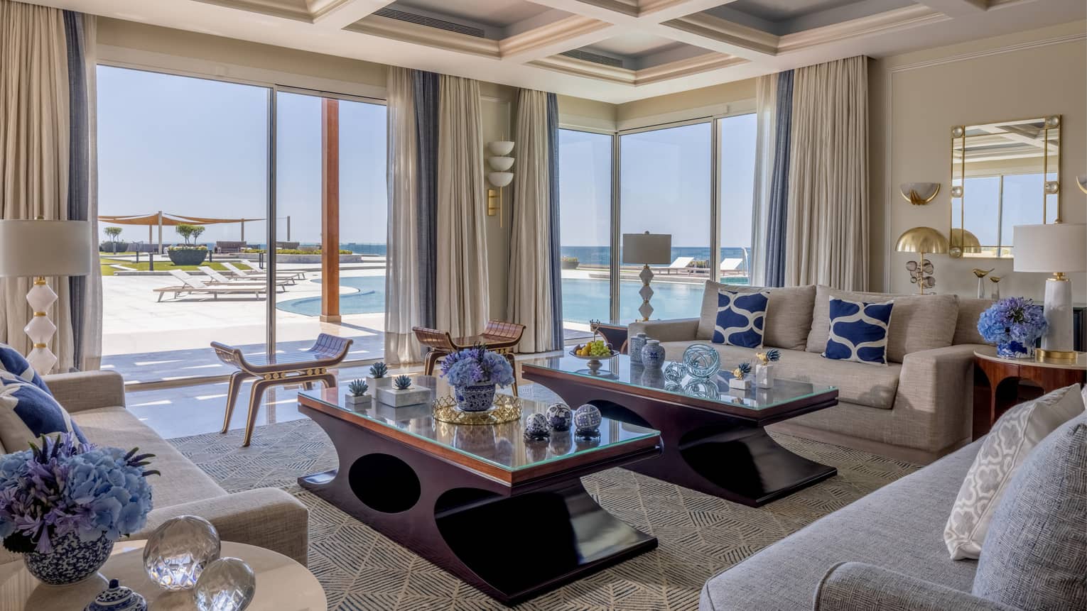 The Palace living area with cream and tan sofas, ergonomic cherry wood coffee tables, sliding glass doors to patio with pool
