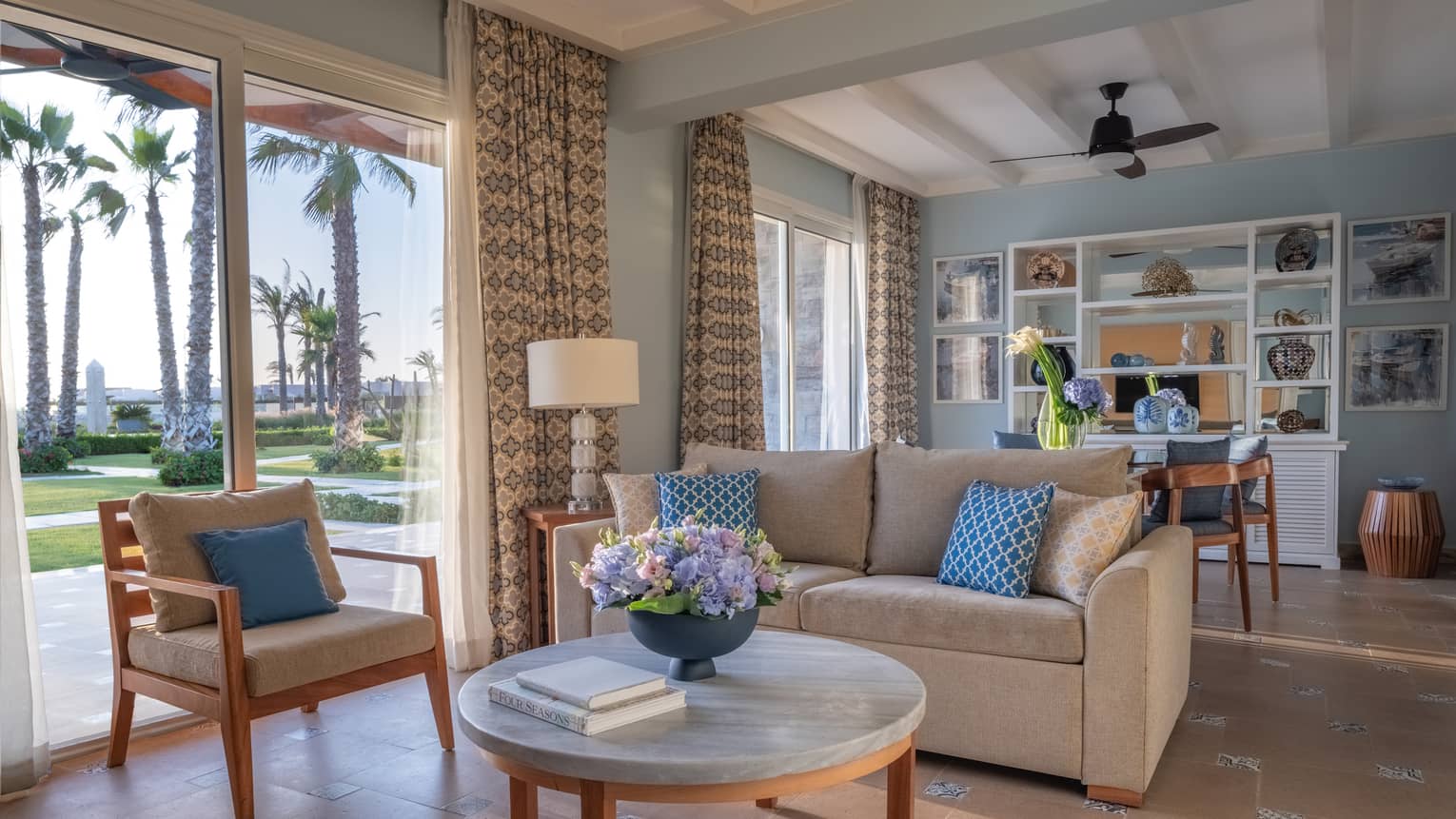 Guest room living area with tan sofa, armchair, round marble coffee table, dining table in background, sliding glass door to patio
