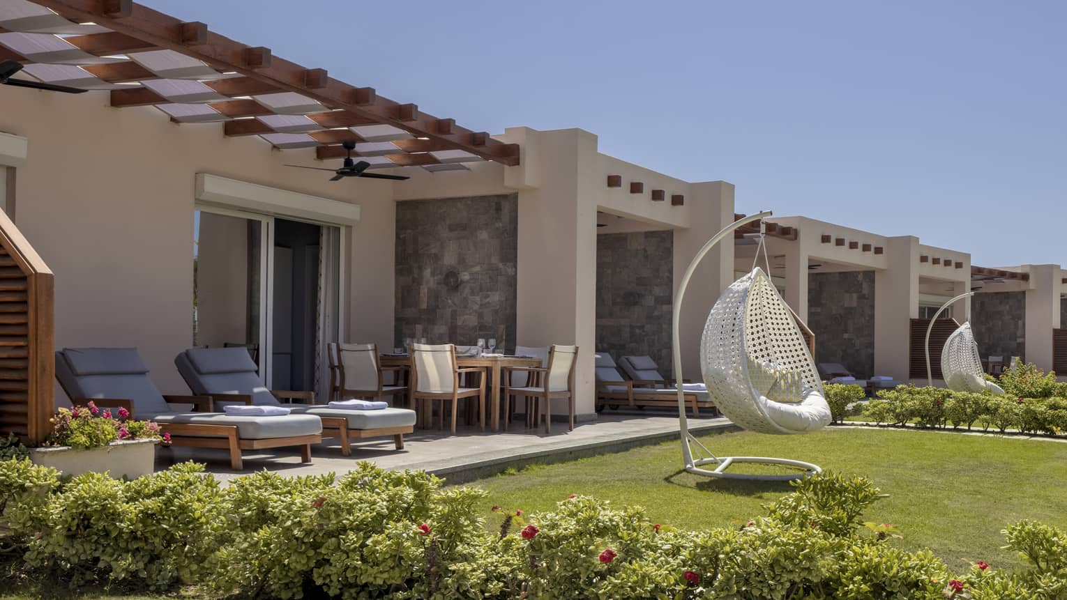 Suite patio and yard with blue lounge chairs and white egg chair, shrubbery