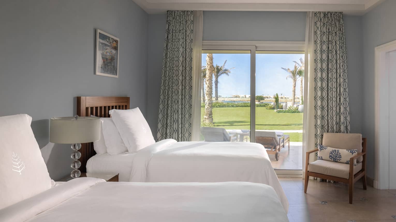 Guest room with twin beds and white linens, tan armchair in corner, sliding glass door to patio