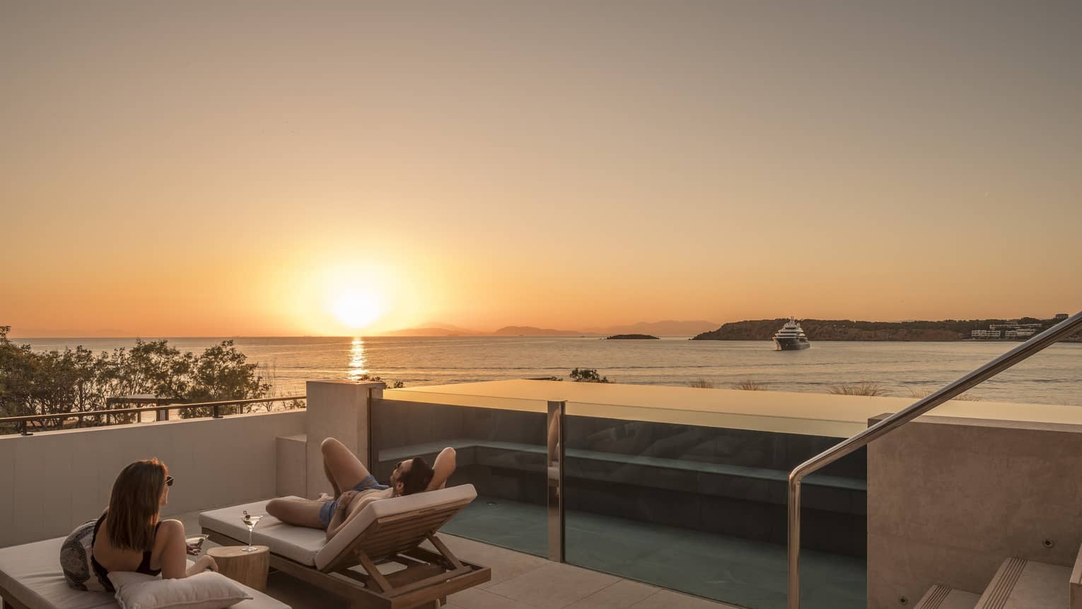 Couple relaxes on plush lounge chairs on Nafsika One Bedroom Terrace Suite with Pool deck