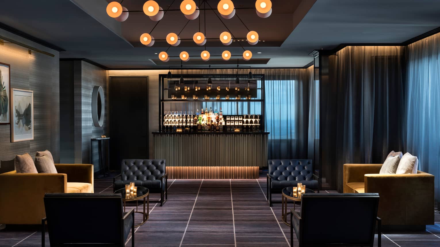 Dimly-lit Penthouse Ballroom with lounge sofas, chairs in front of small bar, under modern lights