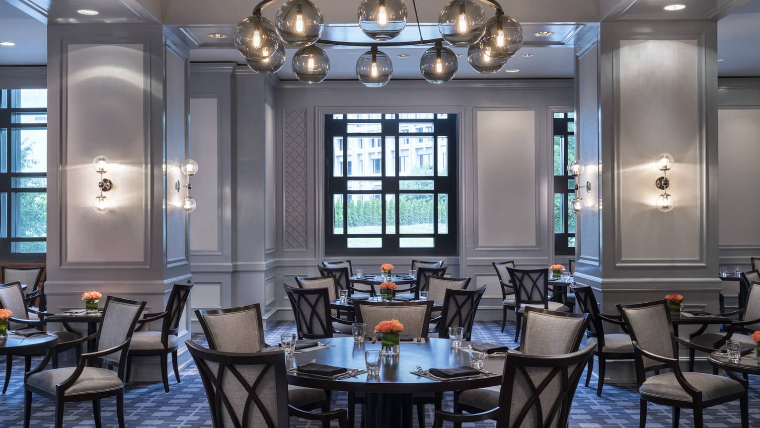 Park 75 dining room with round tables, chairs under grey columns, modern bulb lights