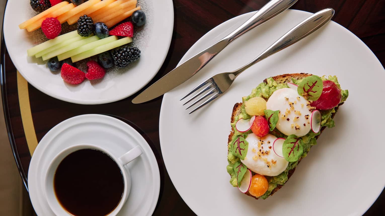 Avocado toast and fruit on white plates.