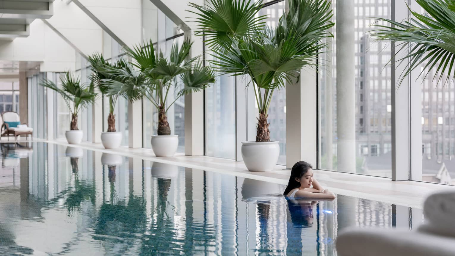 Female guest in sparkling pool surrounded by potted palms and floor-to-ceiling windows