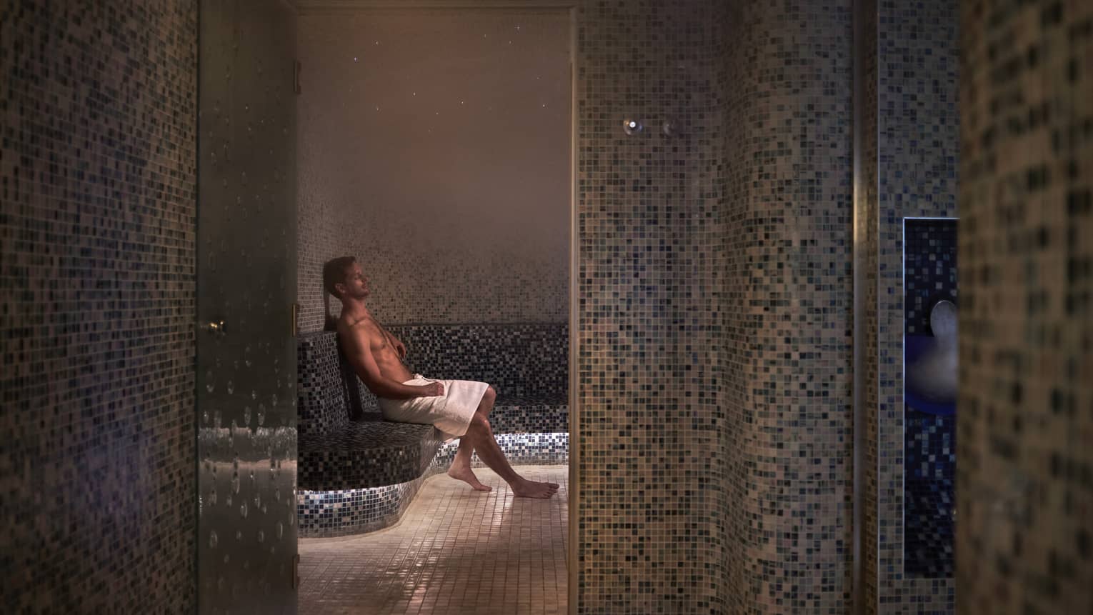 A man sitting with a towel in a dimly lit spa room.