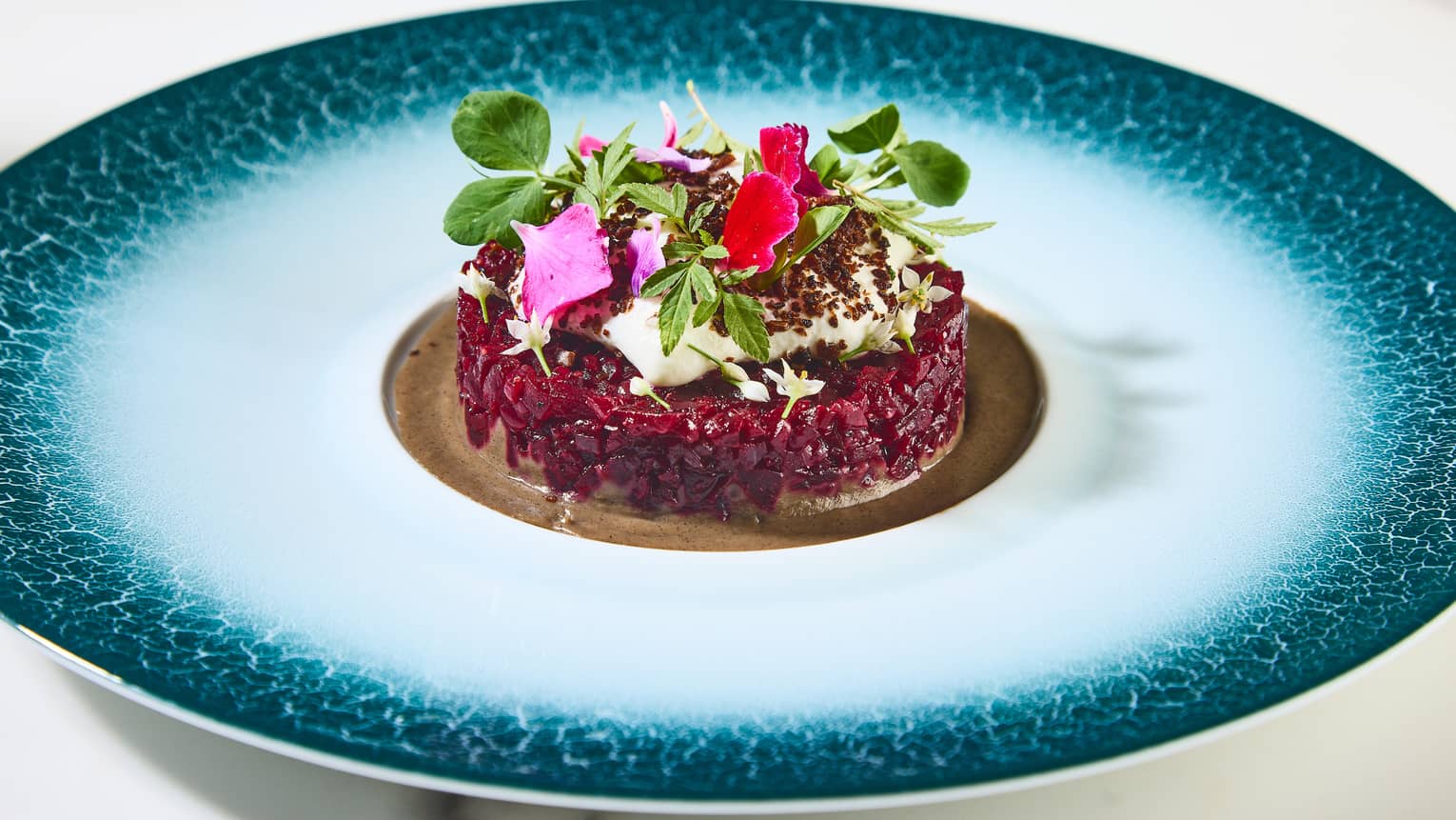 Beetroot tartare with edible flowers and leafy greens as toppings.