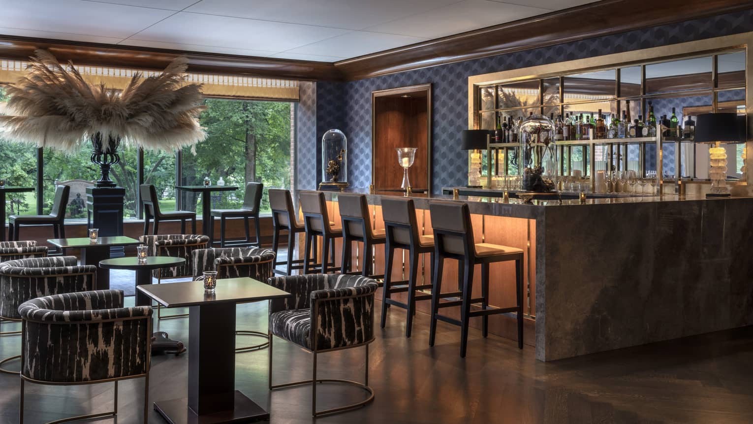 A dining area with small tables and a large bar with black stools.