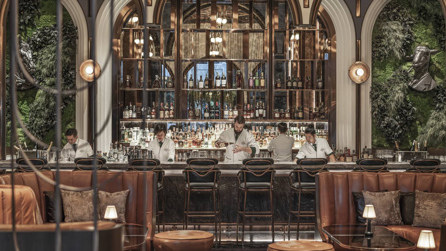 Chic bar with leather seating, plants on the walls and a well-stocked backlit bar, where bartenders in white jackets prepare drinks behind the counter.