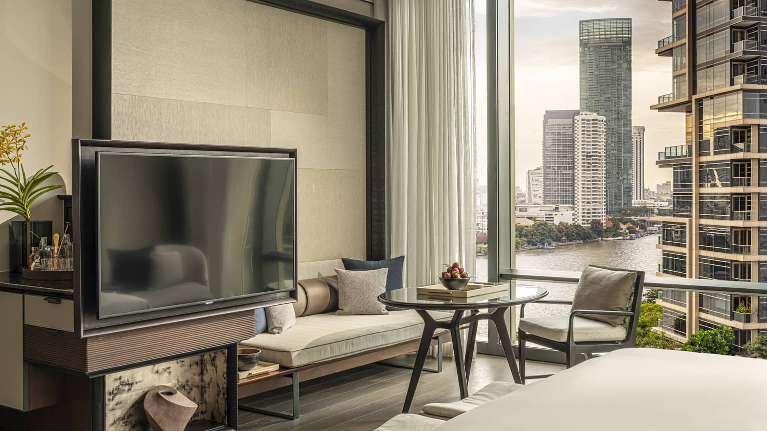 Hotel room with TV, sofa, chair and table with window wall