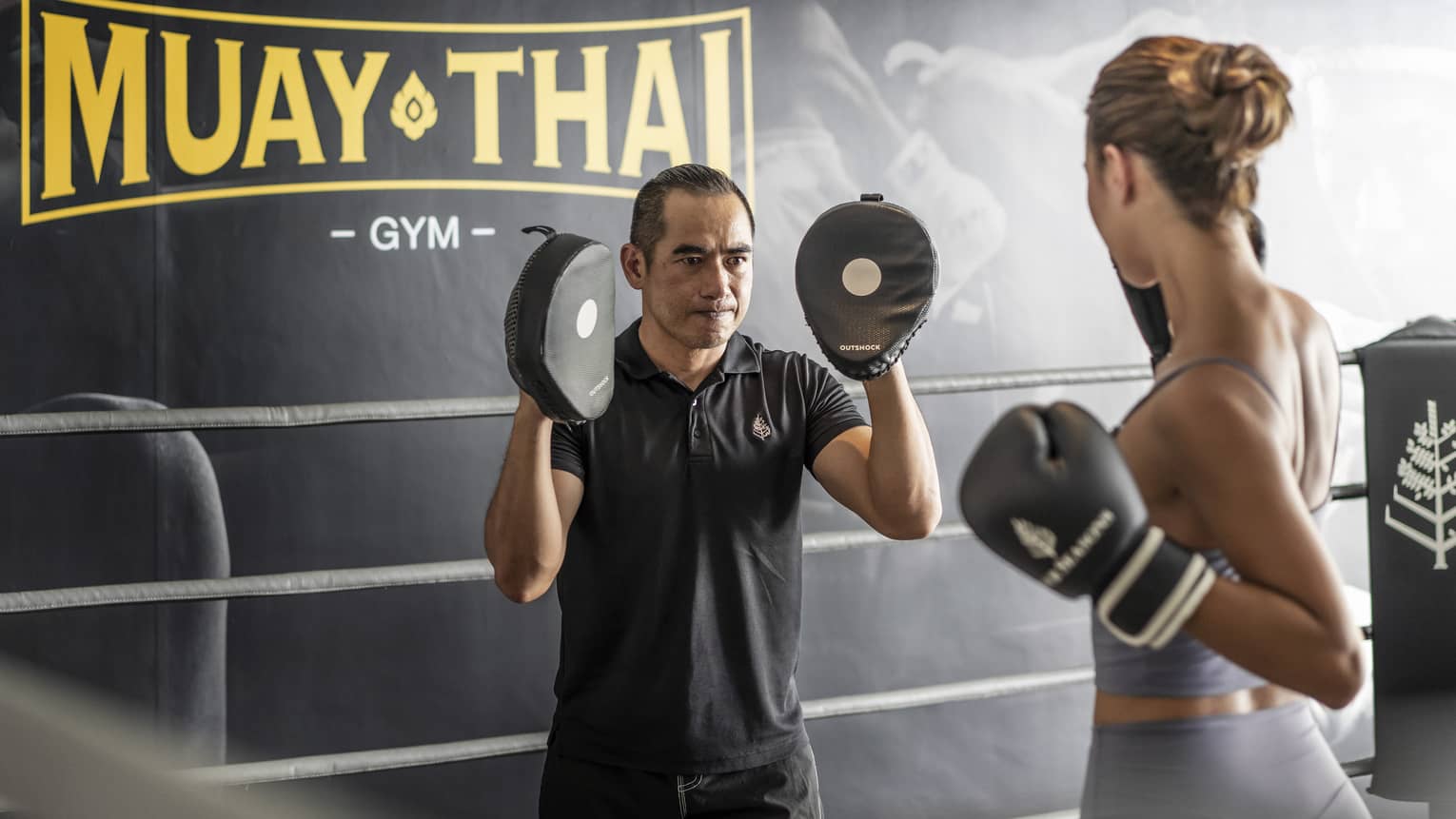 Woman practices Muay Thai with instructor in the ring of a gym