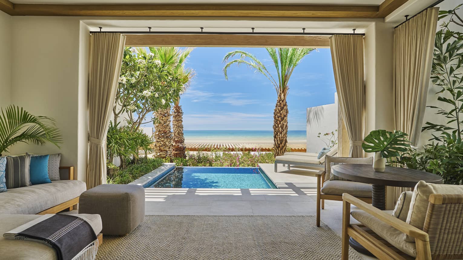 Luxurious ocean-view casita room with a plunge pool, surrounded by greenery and palm trees and featuring comfortable indoor seating and a table