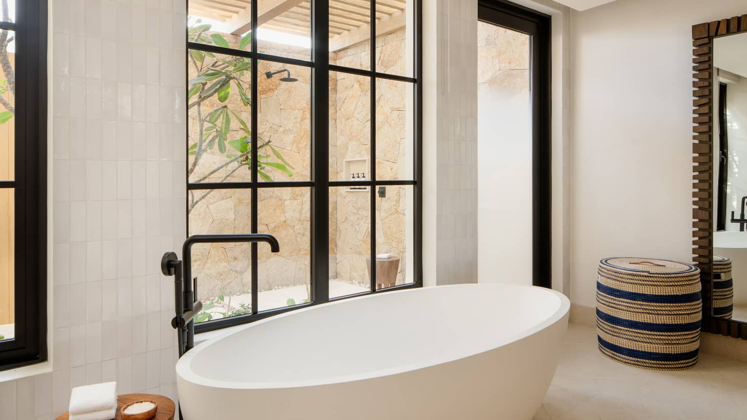 Luxury resort bathroom with standalone oval tub next to an outdoor shower window
