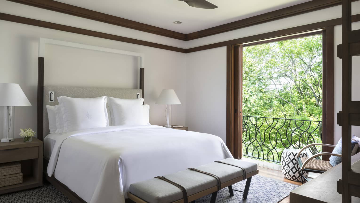 Canopy Suite poster bed with white linens, modern grey bench at foot by open sliding wood doors to sunny terrace