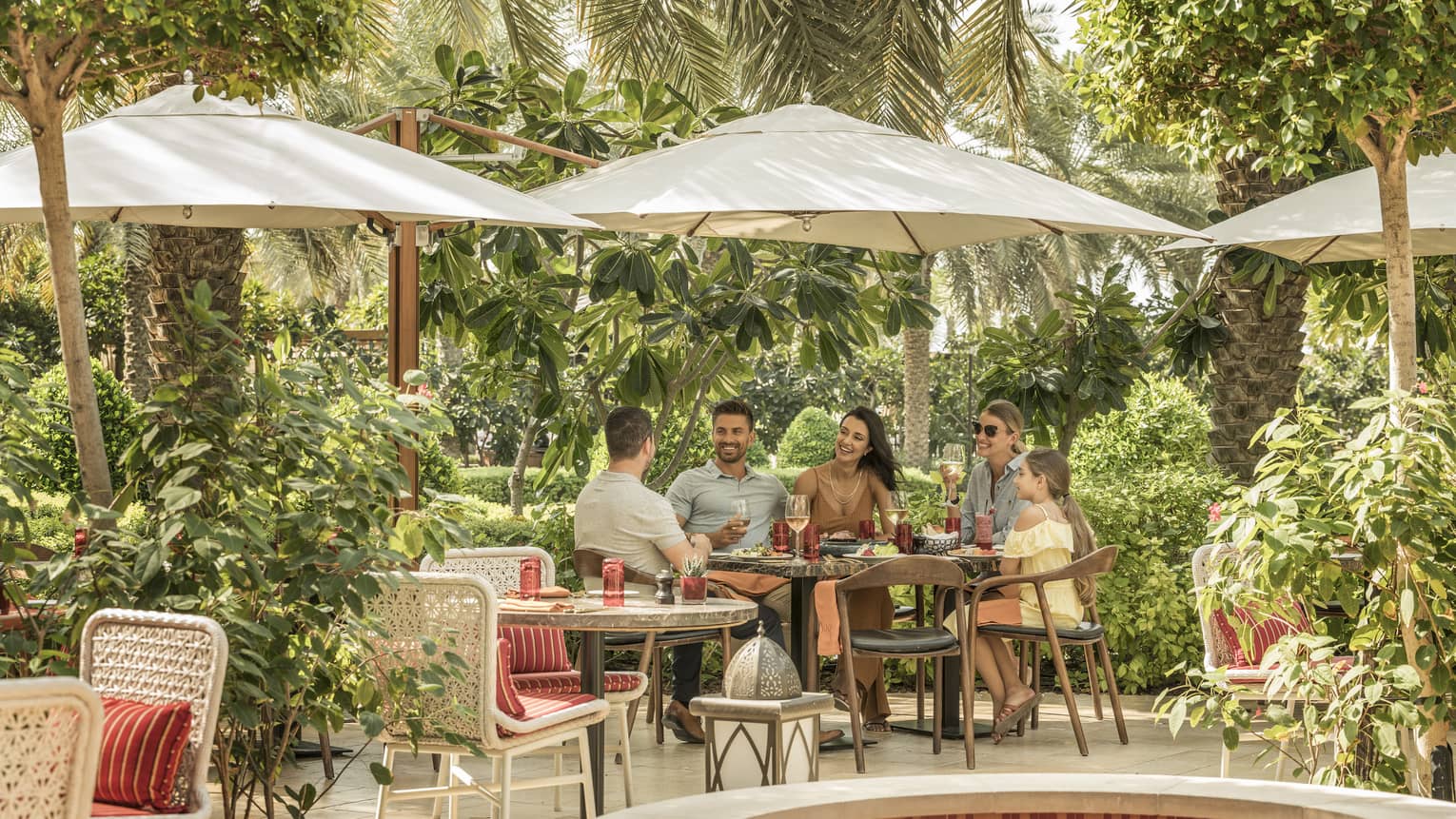 Two couples and a child dine outdoor under an umbrella on SUK's patio surrounded by trees and vegetation