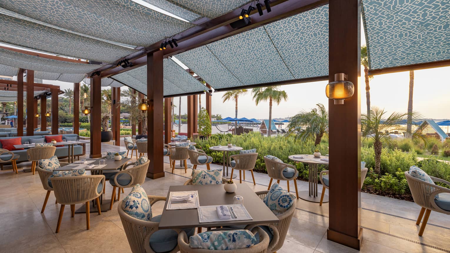 Terrace of restaurant decorated in light blues and greys that looks over a beachfront garden