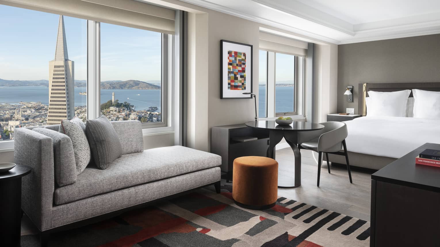 Modern hotel room with queen bed and sofa, overlooking San Francisco and bay