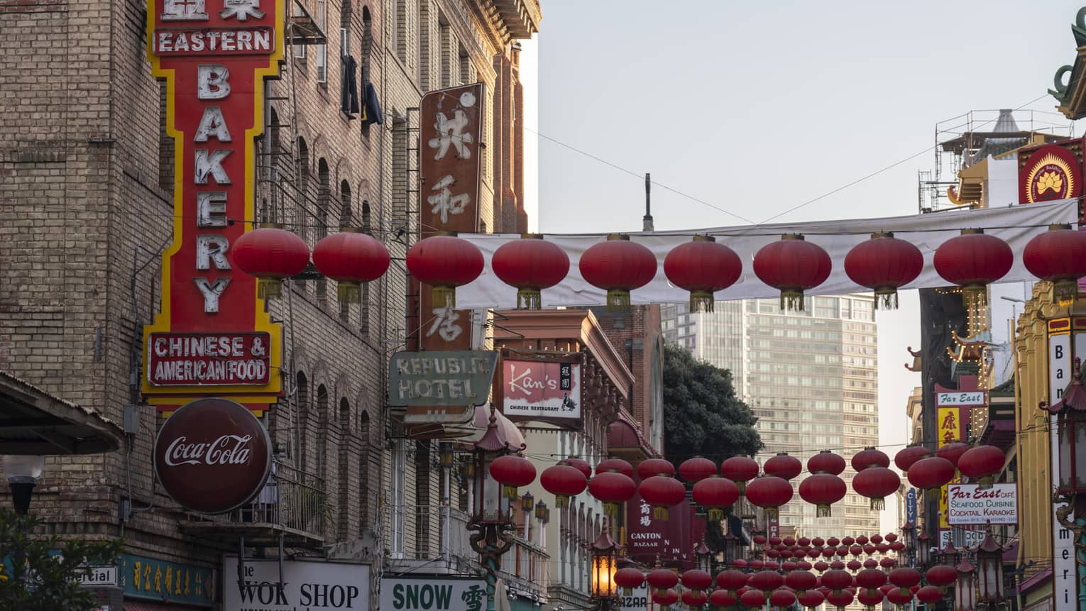 Strings of red lanterns hang across a street in the heart of Chinatown with business signs in English and Chinese characters.