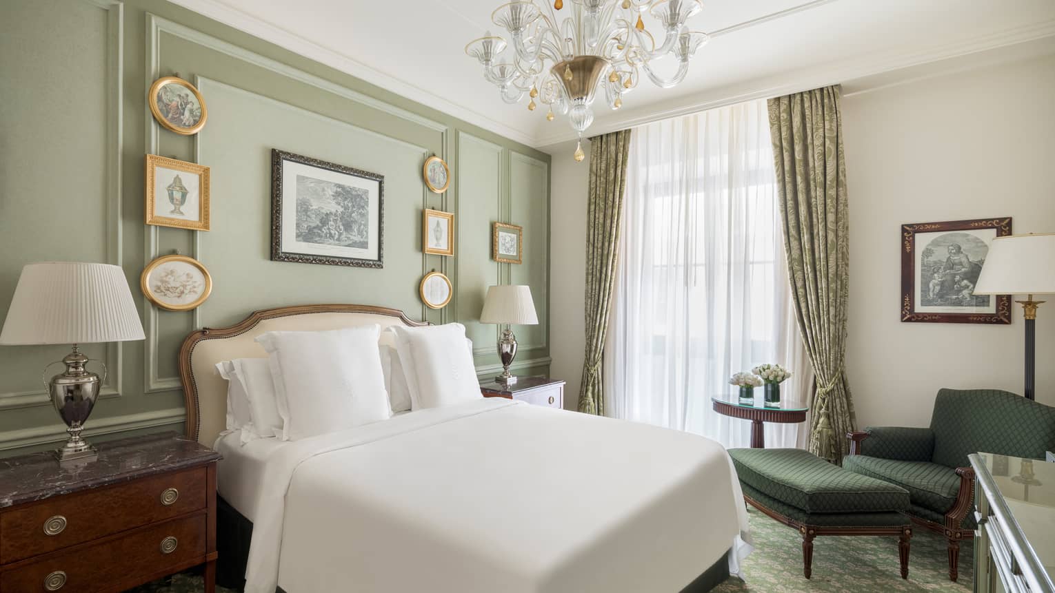 Bedroom with light green walls, small picture frames, crystal chandelier, white king bed