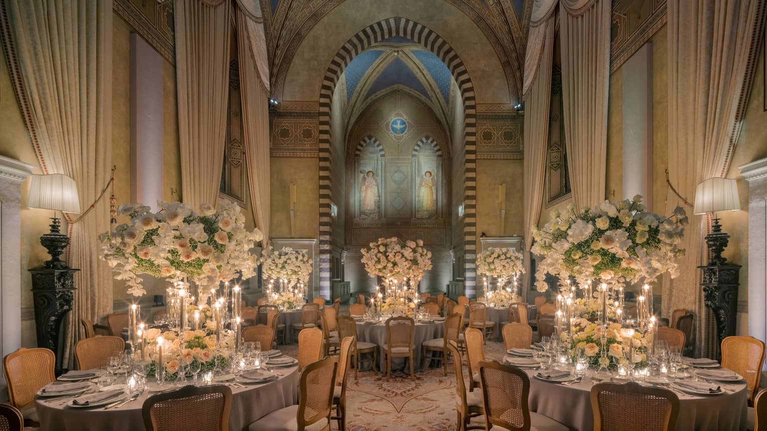 Grand dining room with tall arched ceilings and round elegantly set tables with tall white flower centrepieces